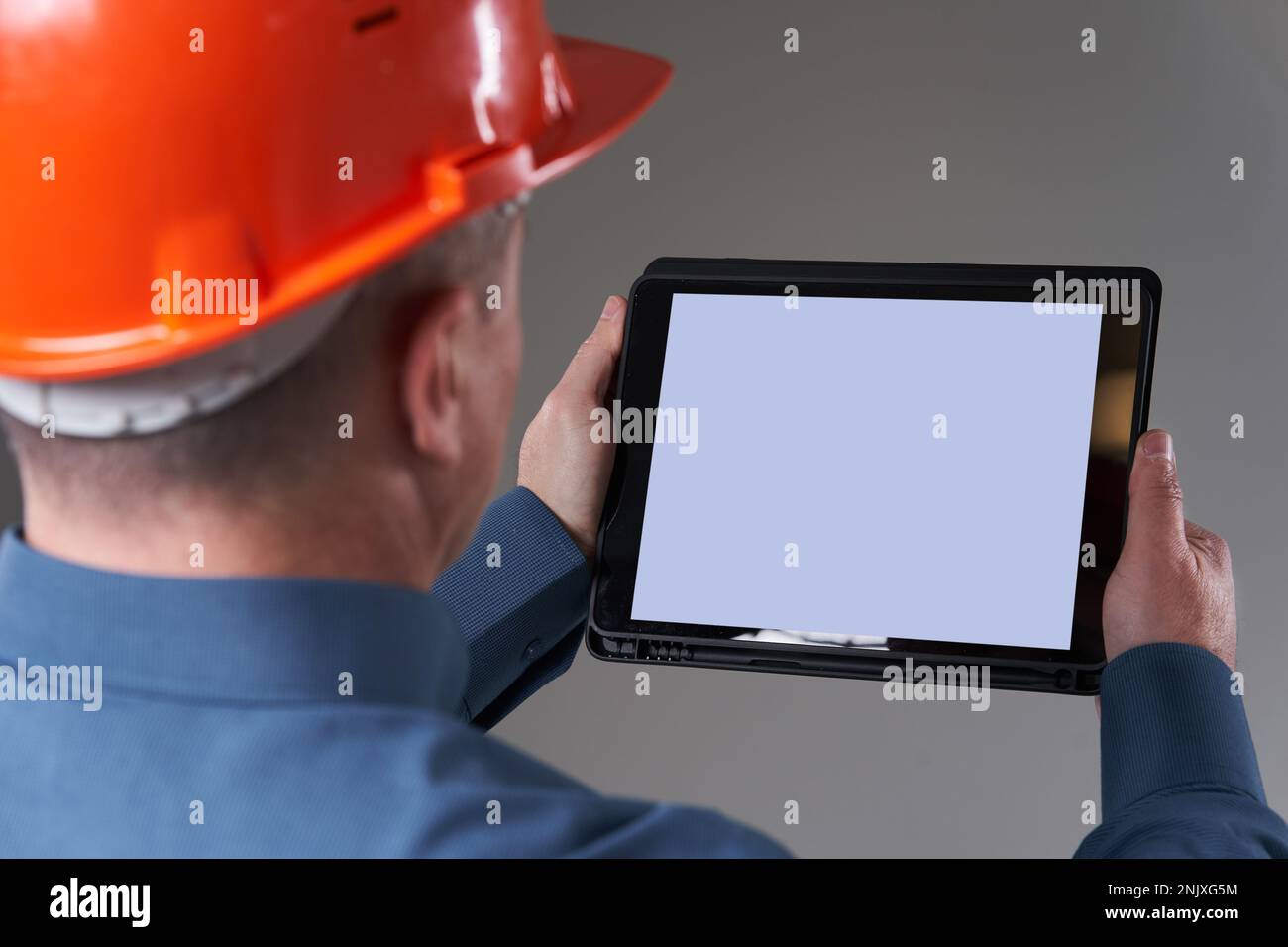 Engineer in hardhat doing planning digitally with a tablet, isolated on gray background Stock Photo