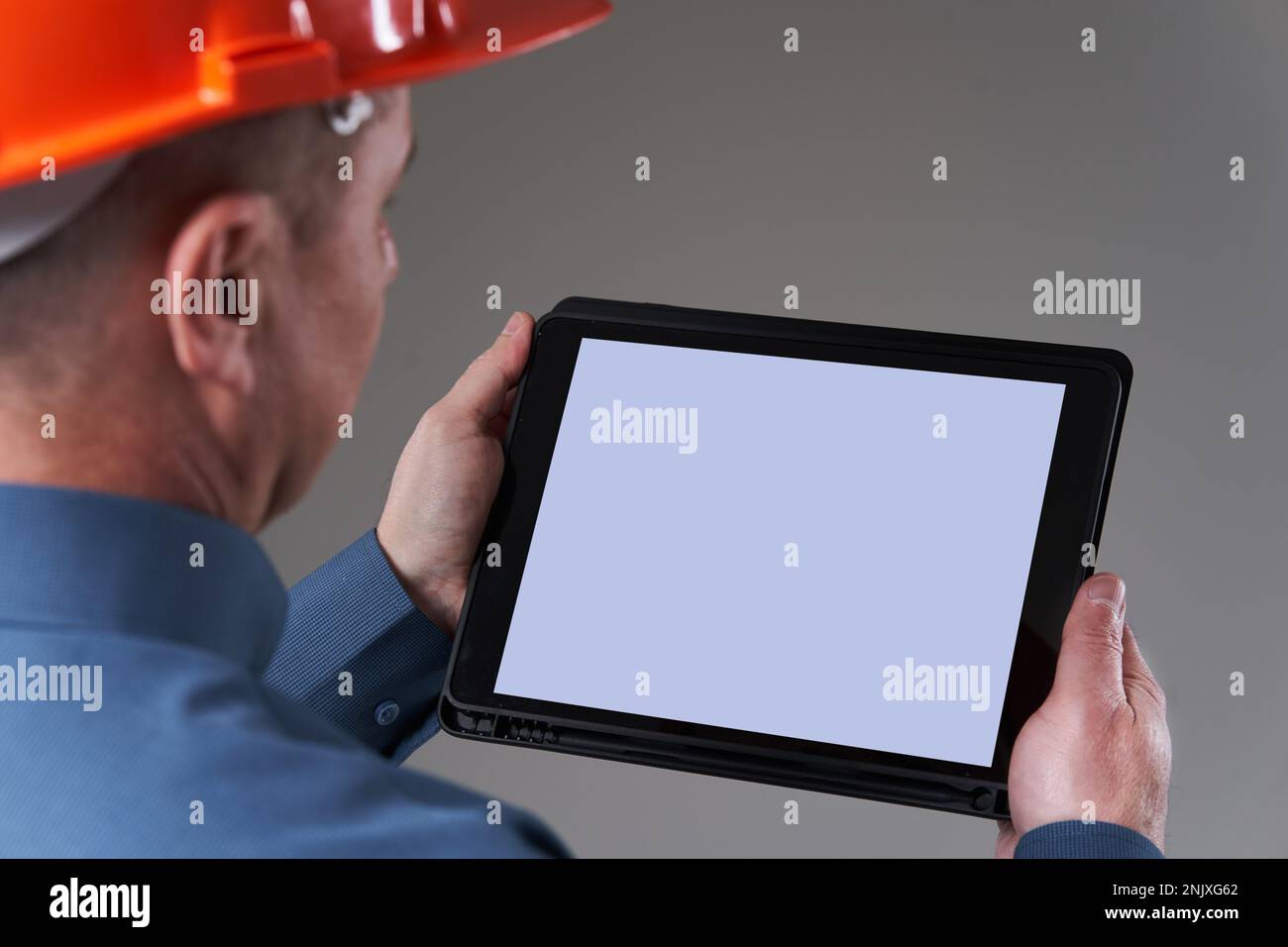 Engineer in hardhat doing planning digitally with a tablet, isolated on gray background Stock Photo
