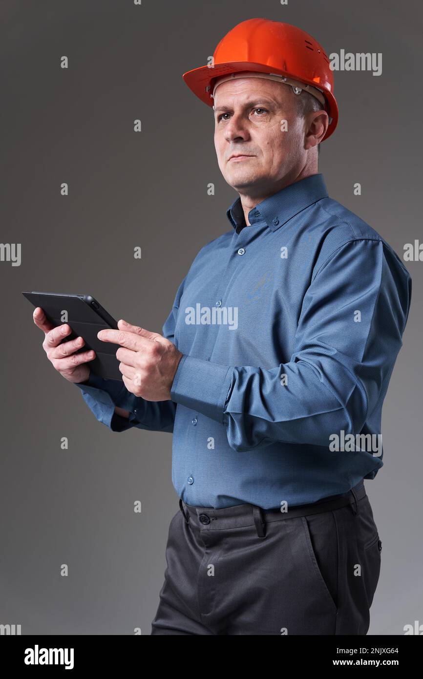 Engineer in hardhat doing planning digitally with a tablet, isolated on gray background Stock Photo