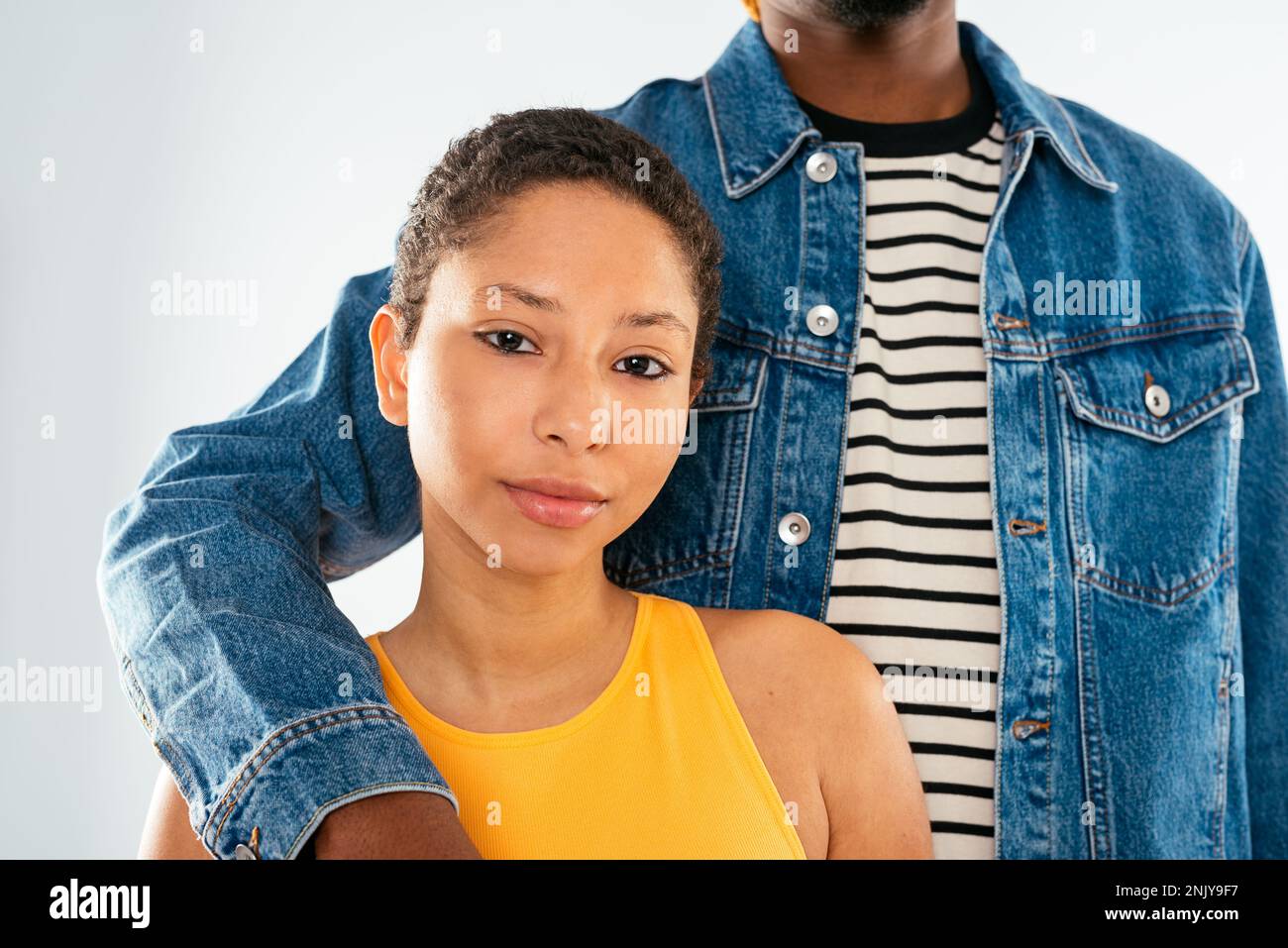 Cropped unrecognizable African American boyfriend with dreadlocks in denim jacket hugging girlfriend with short hair in studio Stock Photo