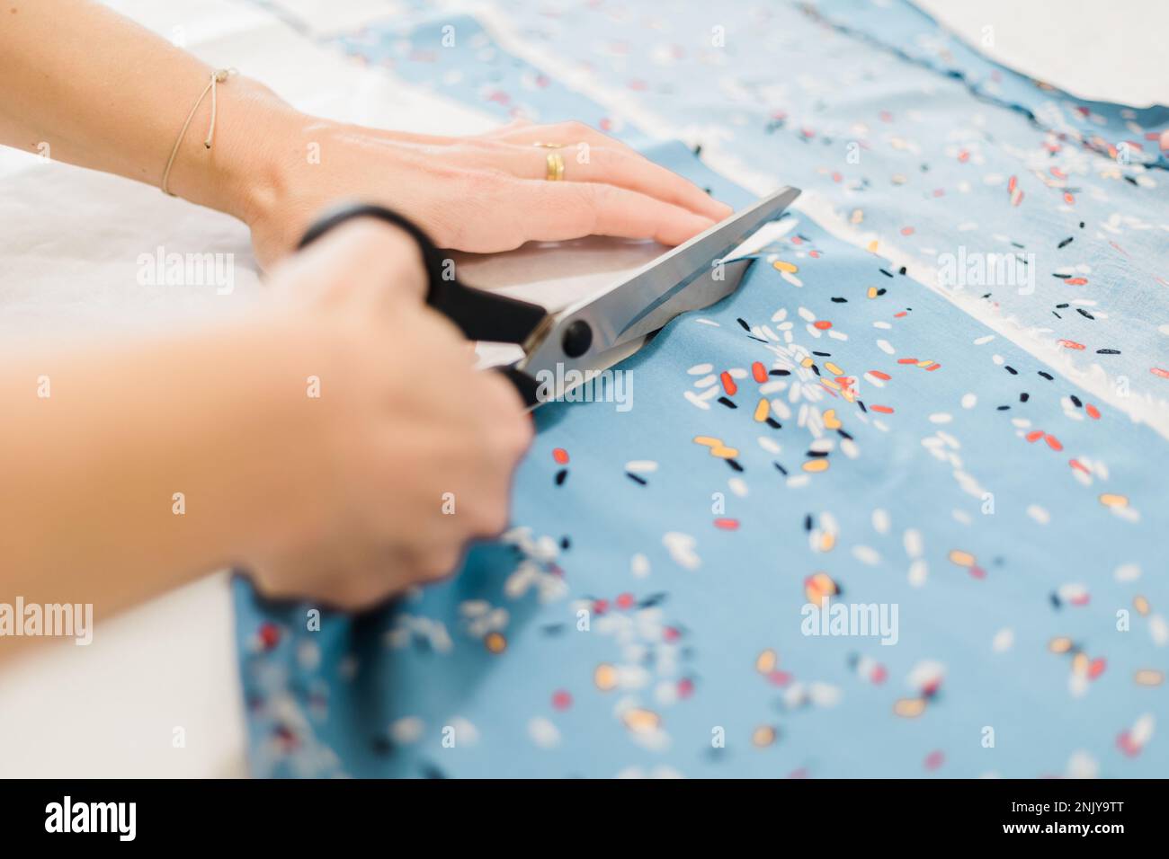 Anonymous designer using scissors to cut fabric while working in atelier with patterns Stock Photo