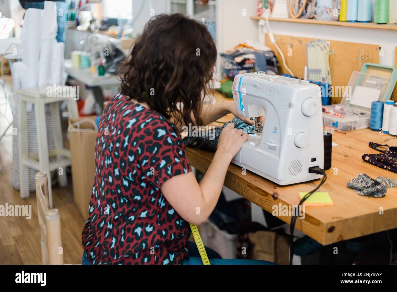 Back view of unrecognizable female tailor putting thread into sewing ...
