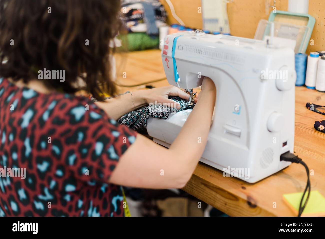 Back view of unrecognizable female tailor putting thread into sewing ...