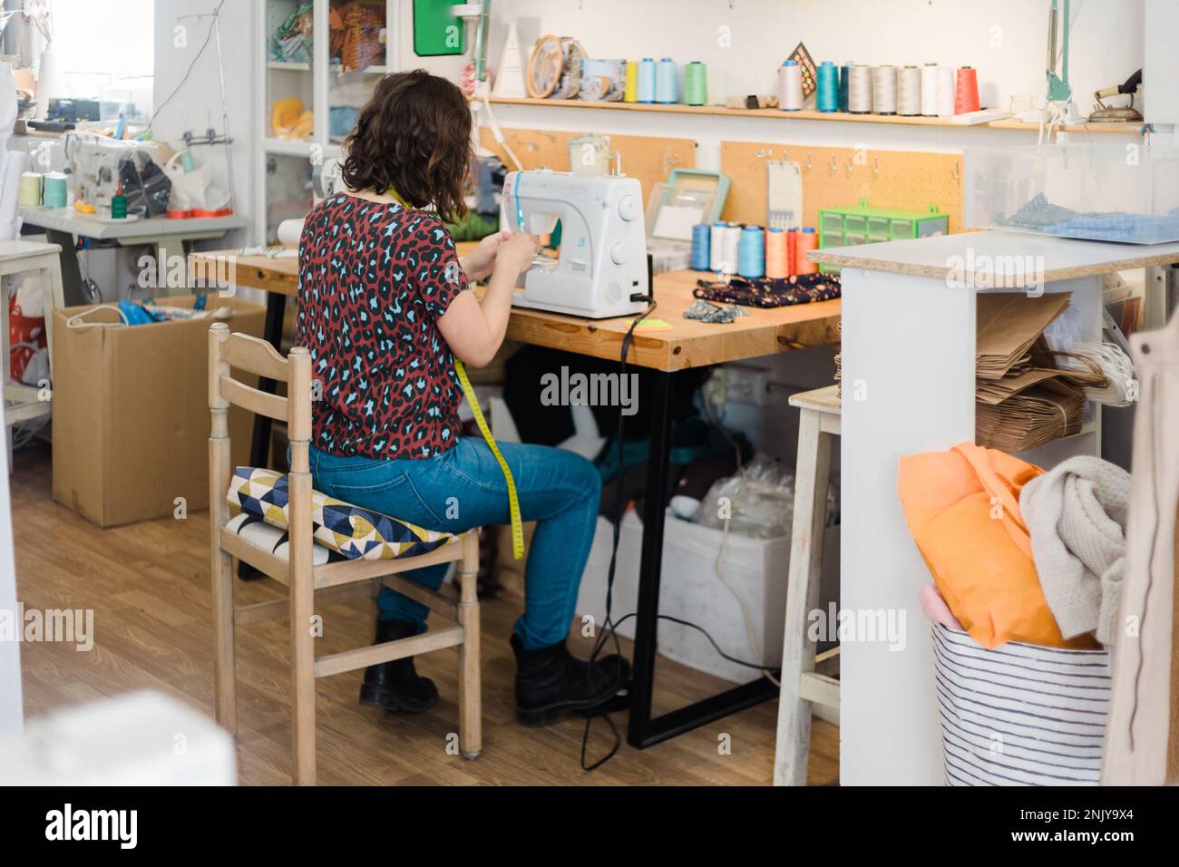 Back view of unrecognizable female tailor putting thread into sewing ...