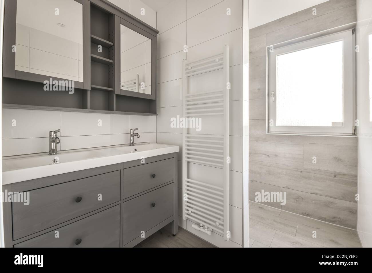 Gray with sinks and cupboard with mirrors located near towel dryer in modern bathroom