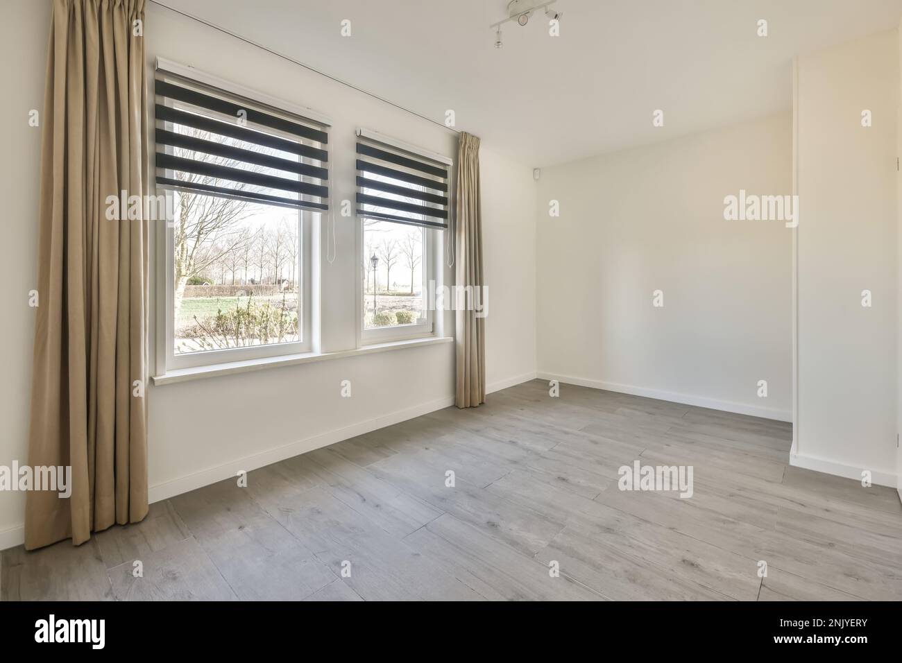Windows with curtains on white wall of sunlit empty room of new house in daytime Stock Photo