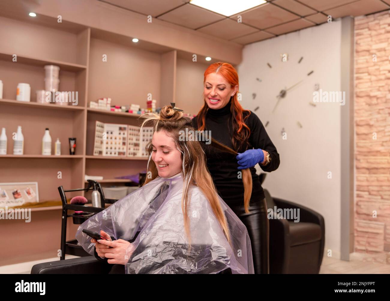 Cheerful female hairdresser in latex gloves dying hair of happy client