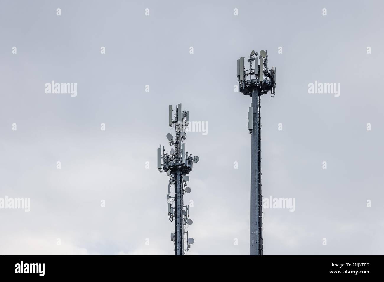 Two cell towers with different antennas and signal boosters against a cloudy sky Stock Photo
