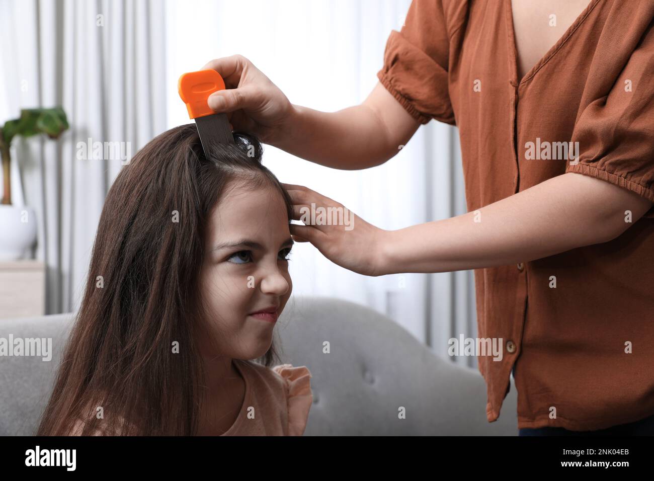 Mother using nit comb on her daughter's hair indoors. Anti lice