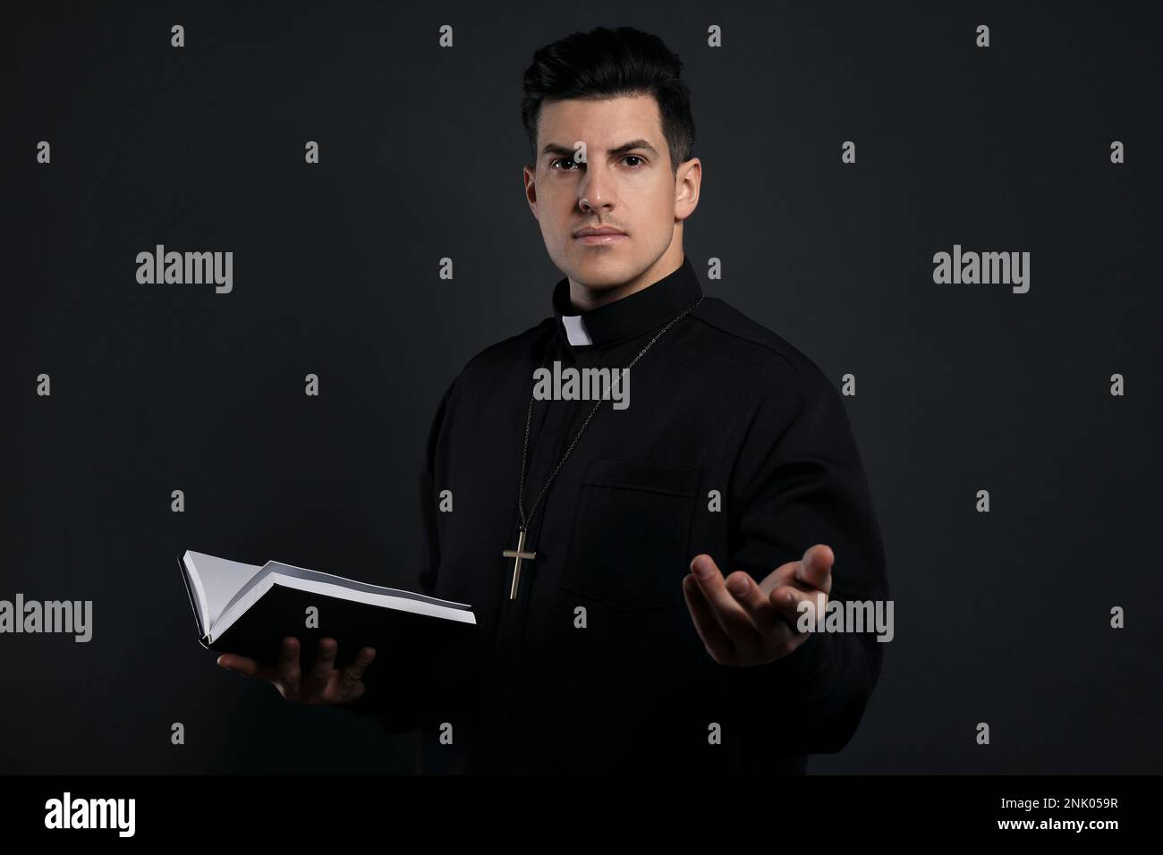 Priest in cassock with Bible on black background Stock Photo