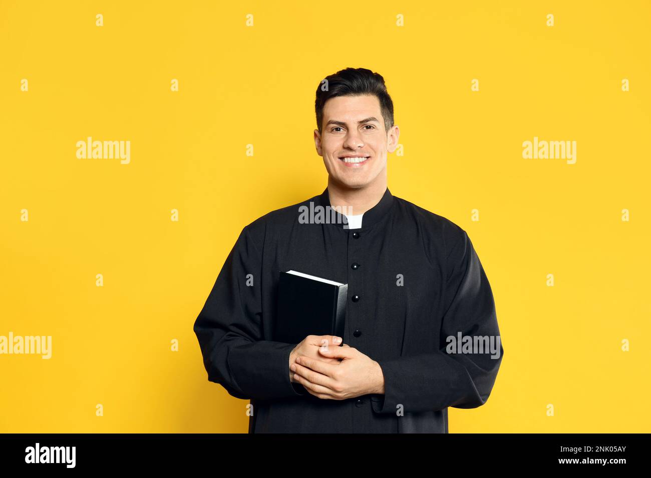 Priest in cassock with Bible on yellow background Stock Photo