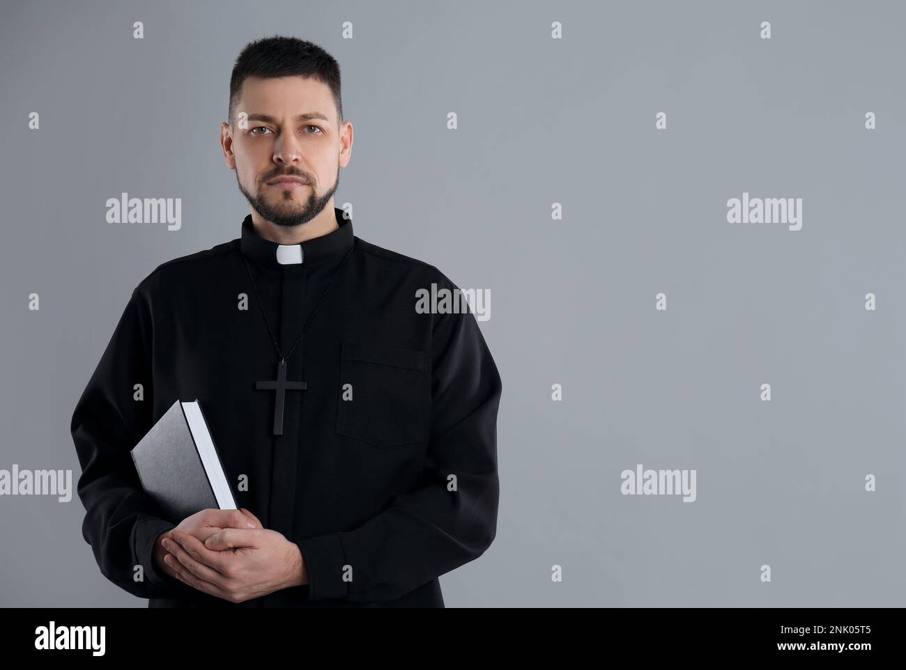 Priest with Bible on grey background, space for text Stock Photo