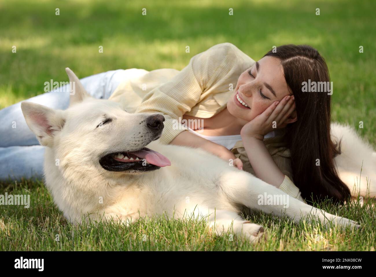 Teenage girl lying with her white Swiss Shepherd dog on green grass in ...