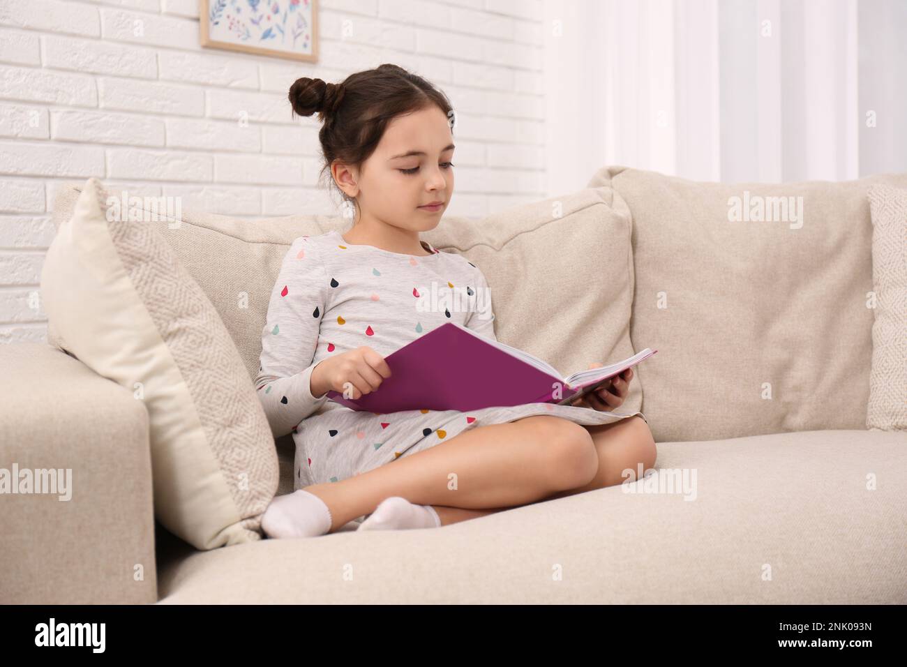 Little girl reading book on sofa at home Stock Photo - Alamy