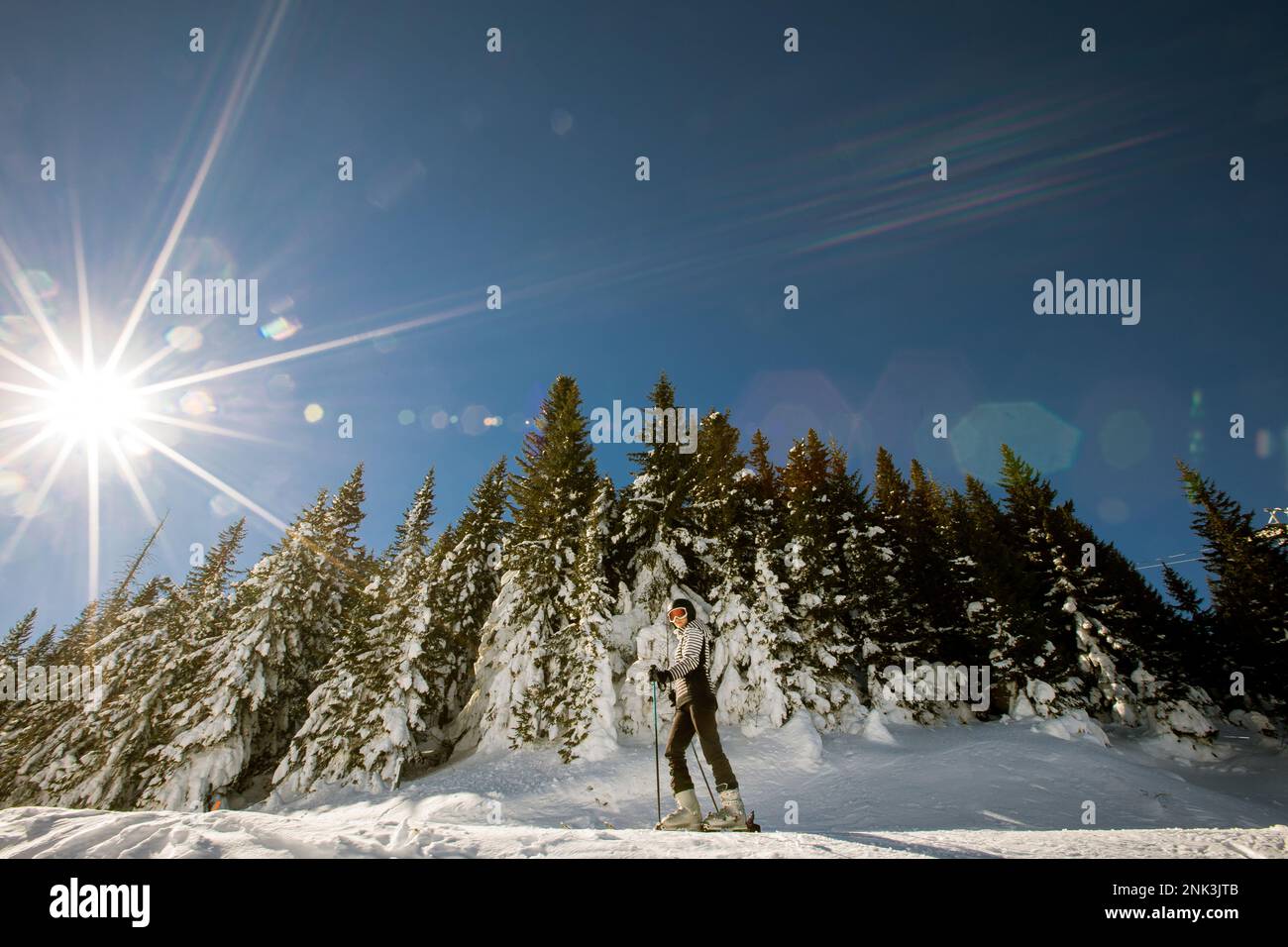 A single young female enjoys a sunny winter day of skiing, dressed in full snow gear with ski boots and sunglasses Stock Photo