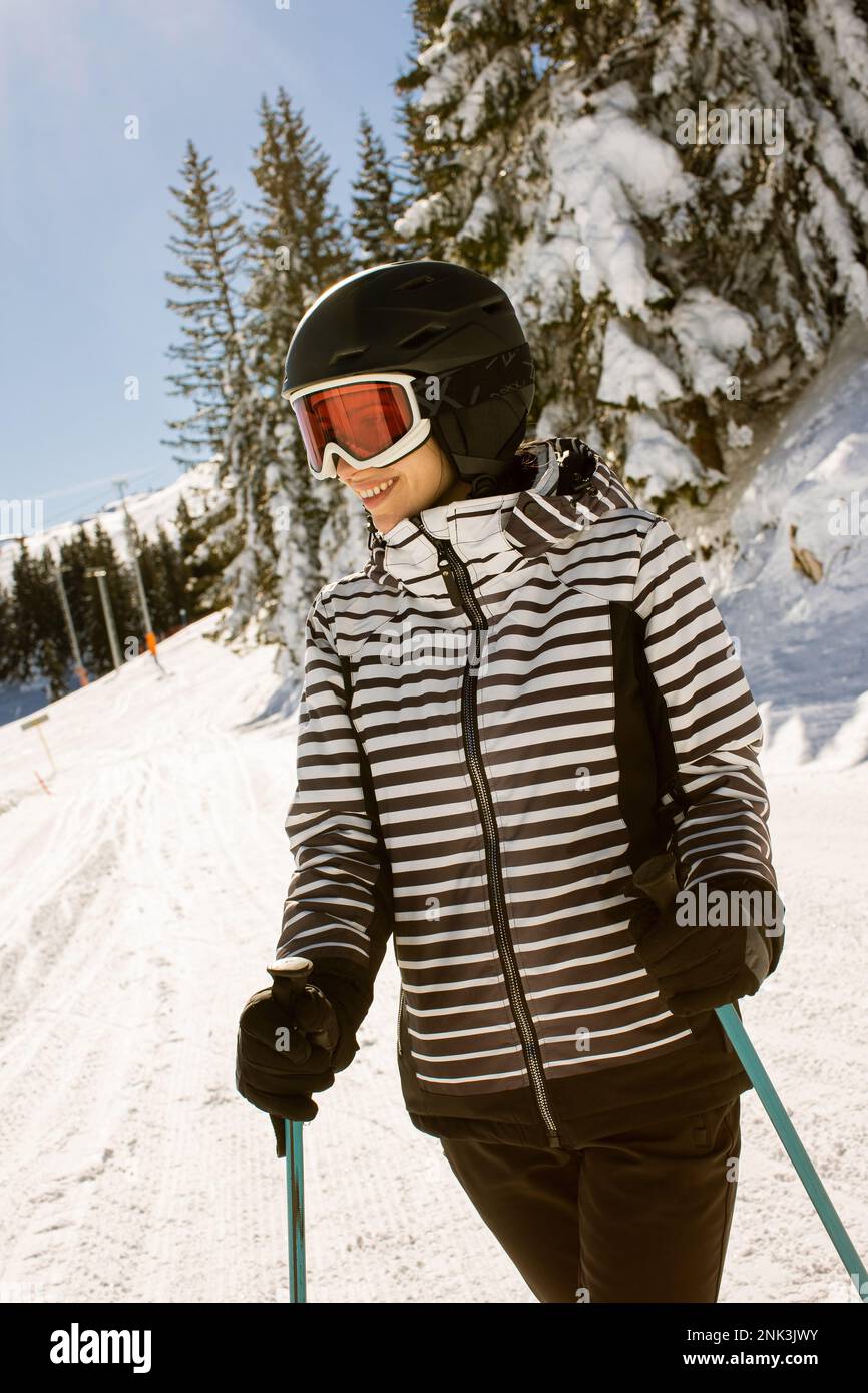 Young woman enjoying winter day of skiing on the snow covered slopes, surrounded by tall trees and dressed for cold temperatures Stock Photo