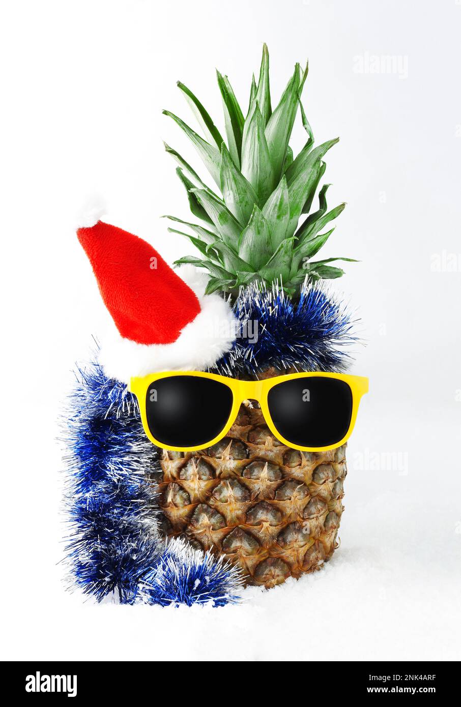 Pineapple tropical fruit in a suit Santa Claus hat and yellow sunglasses on the snow. Isolated on a white background. Concept postcard for New Year an Stock Photo