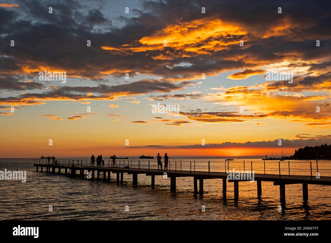 Jetty with tourists silhouetted against sunset over the Adriatic Sea at Ankaran along the Slovenian Riviera, Littoral region of Slovenia Stock Photo