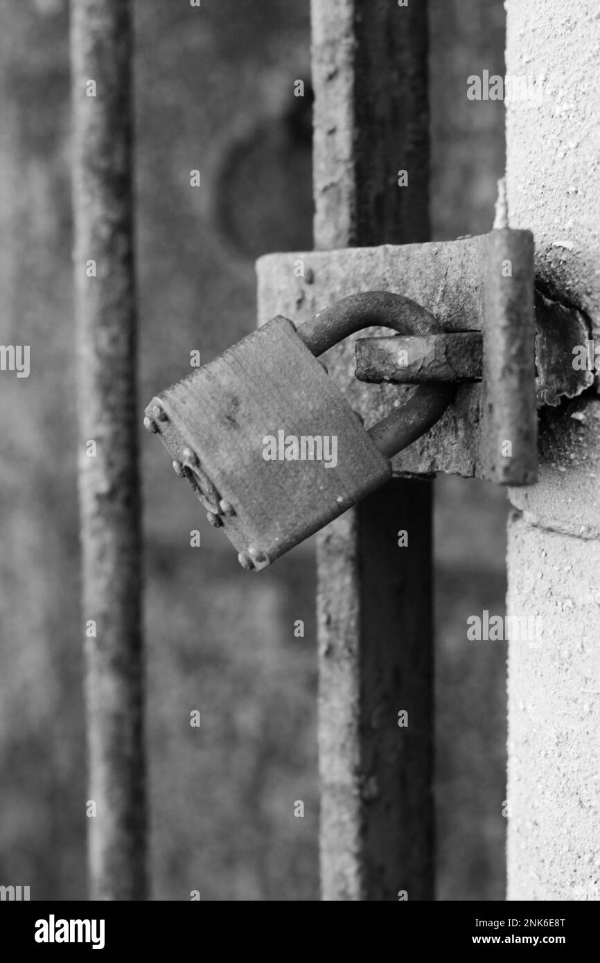 Vintage traditional metal padlock keeping a gate closed in a black and