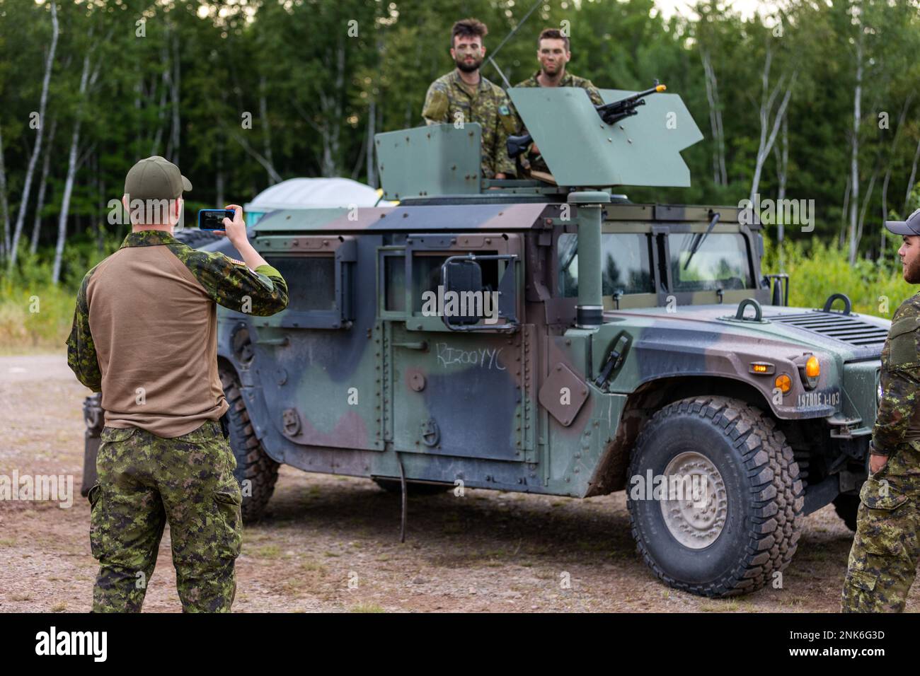 Two Canadian soldiers pose for a picture with a C6 machine gun in the turret ring of and American HMMWV while another soldier the picture on a smart phone. CFB Gagetown, New Brunswick, Canada, August 11, 2022. Stock Photo