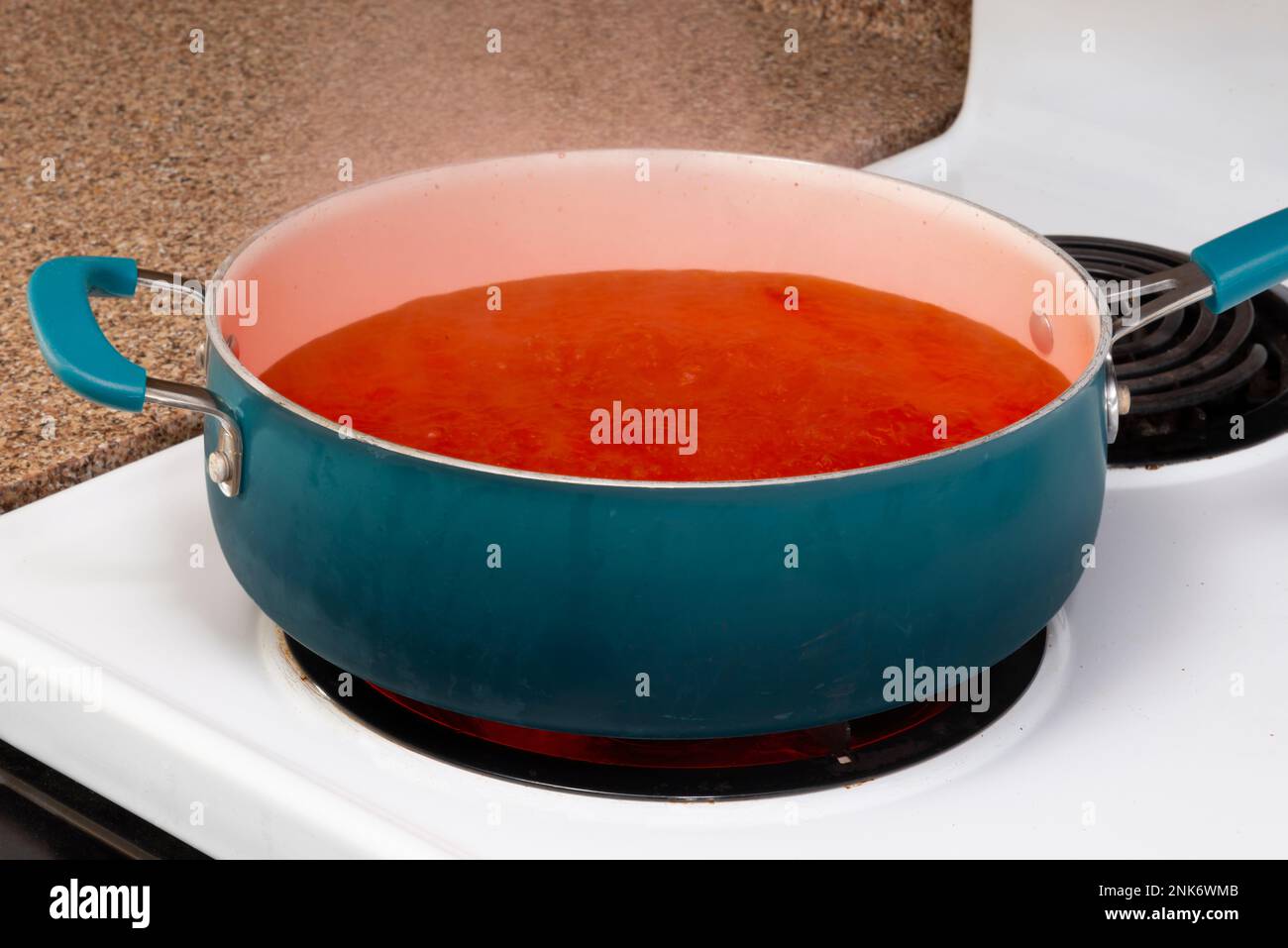 Horizontal close-up shot of a blue pot on a stove top holding steaming tomato soup. Stock Photo