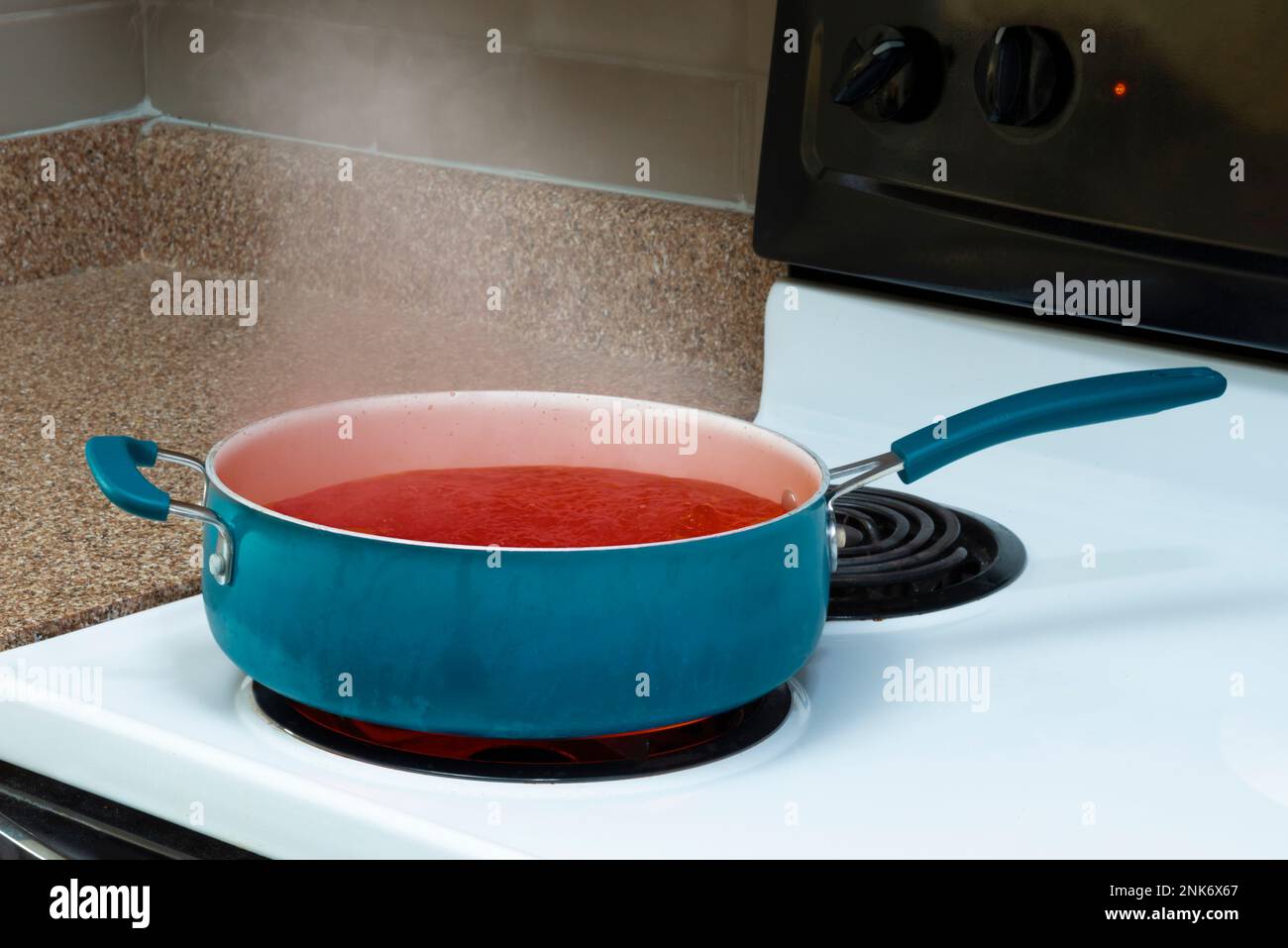 Horizontal shot of a blue pot on a stove top holding steaming tomato soup. Stock Photo