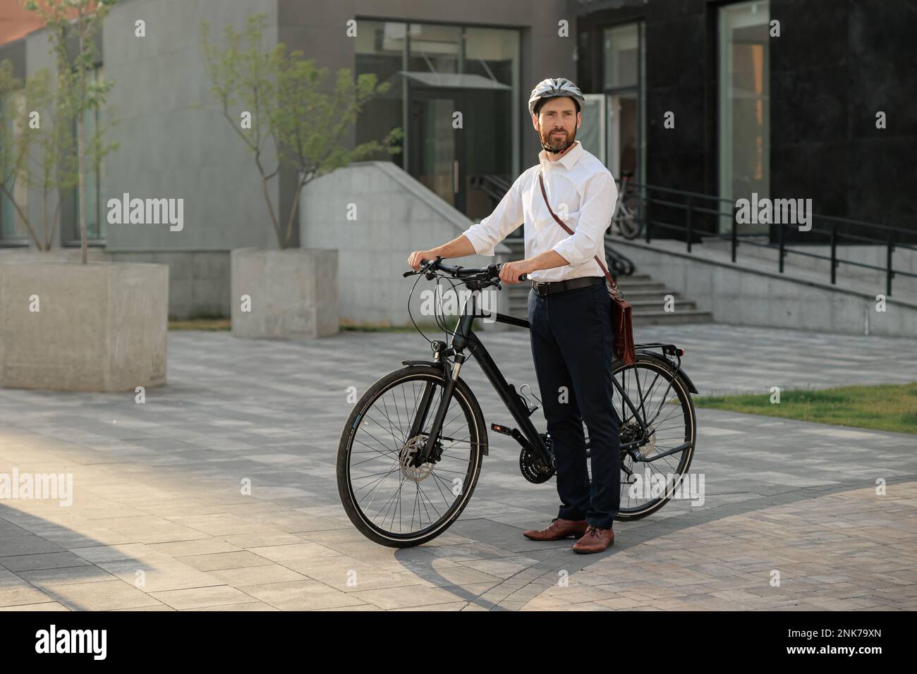 Young businessman commute with bicycle walking home from work in city. Side view of caucasian bearded manager in shirt and helmet standing with modern Stock Photo
