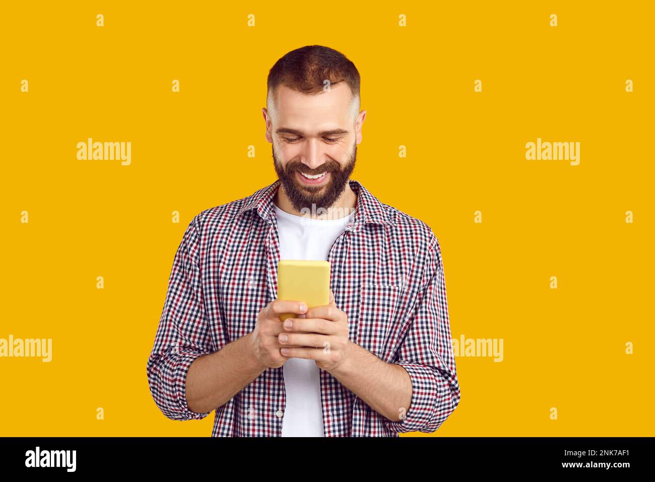 Happy young man in casual shirt looking at his mobile phone, text messaging and smiling Stock Photo