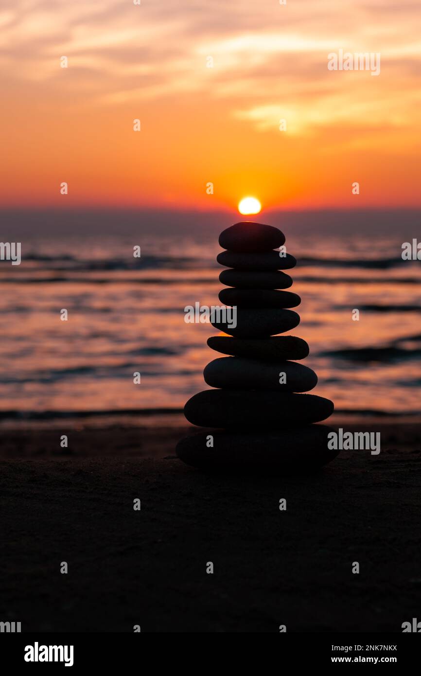 Vertical İmage, Balanced pebble pyramid silhouette on the beach on sunset. Sea on the background. Zen stones on the sea beach, meditation, spa. Stock Photo