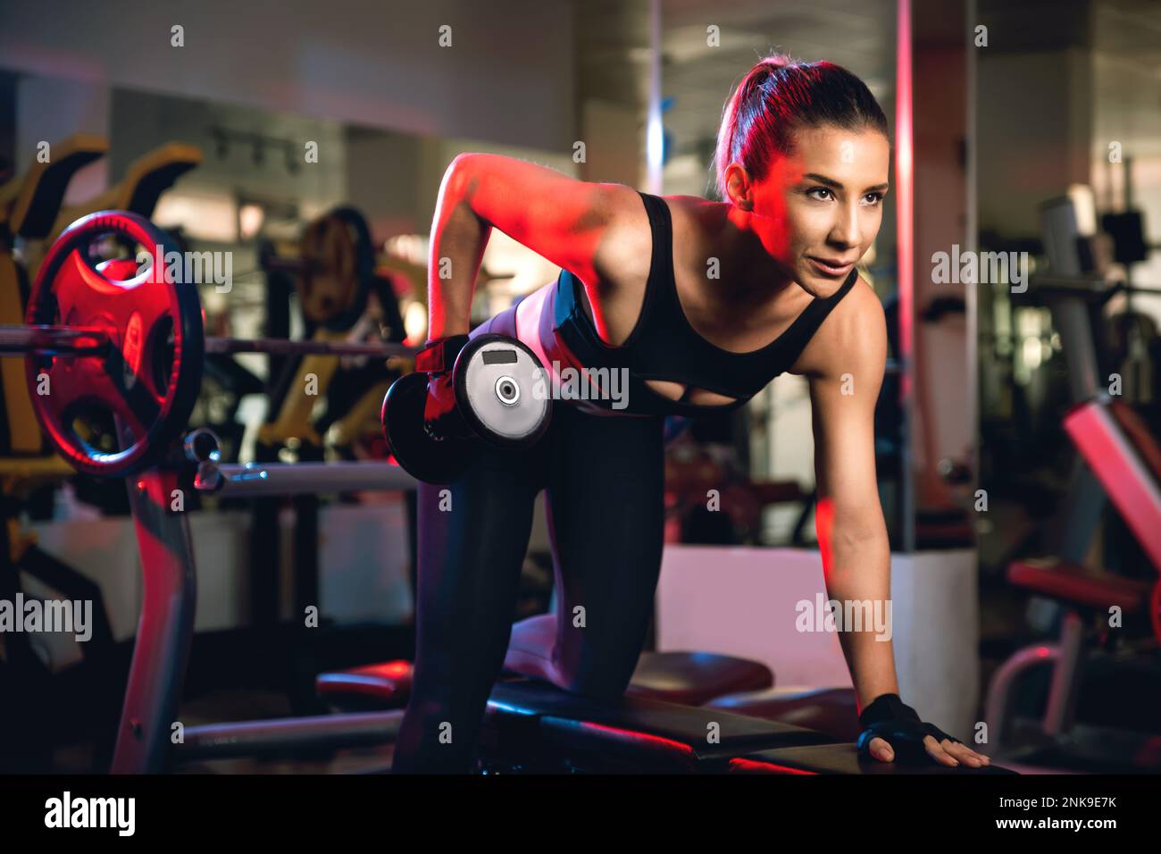 One 30s woman with black tops and tights doing one arm dumbbell lateral workout with dumbbells in a gym. Stock Photo