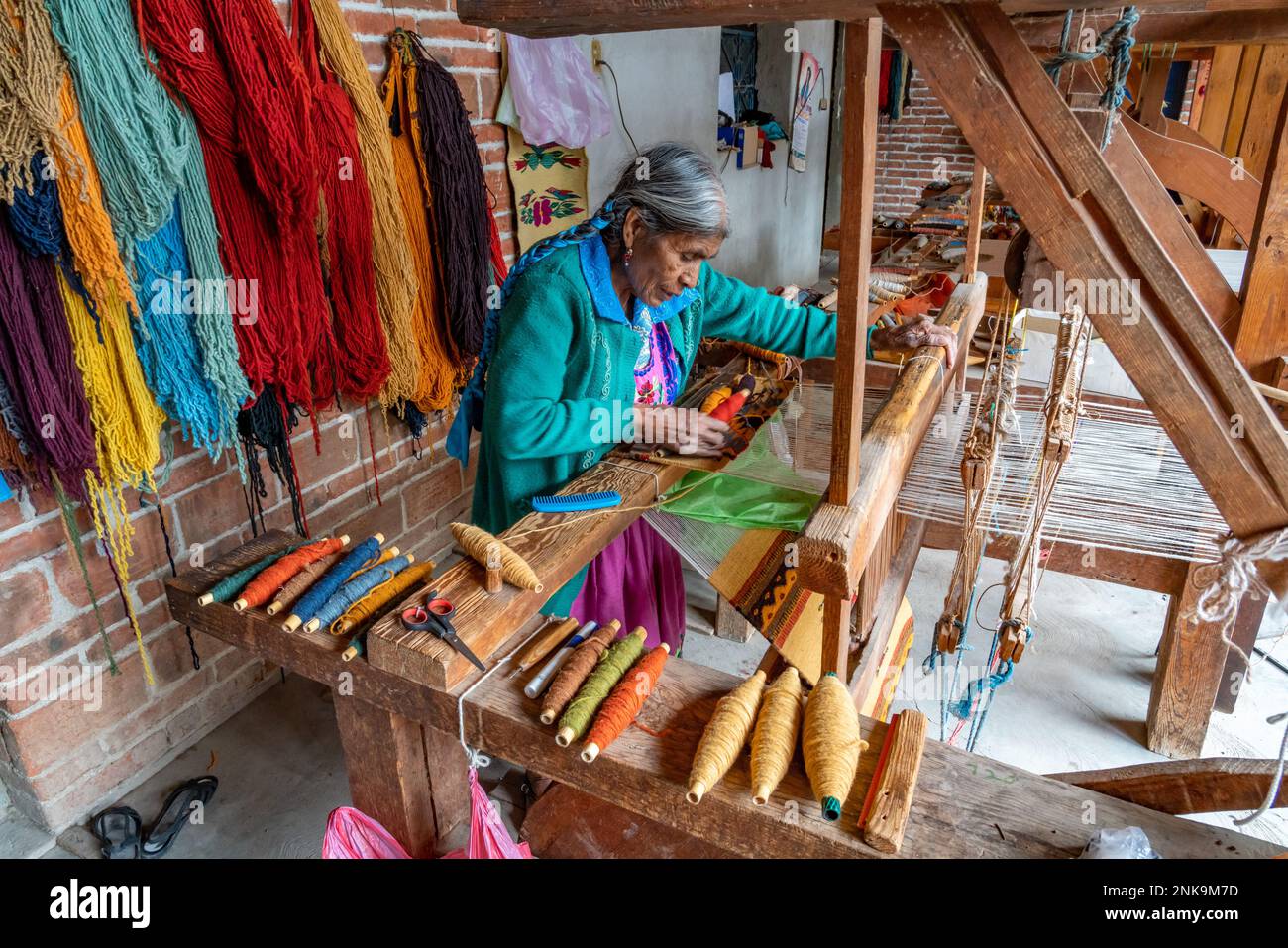 An older indigenous Zapotec woman weaves a woolen rug on a wooden foot