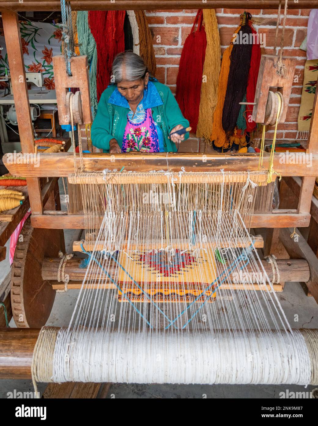 An older indigenous Zapotec woman weaves a woolen rug on a wooden foot