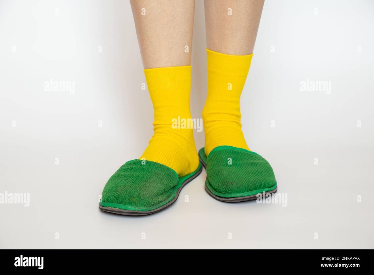 Female legs in yellow socks and green slippers on a white background close -up Stock Photo