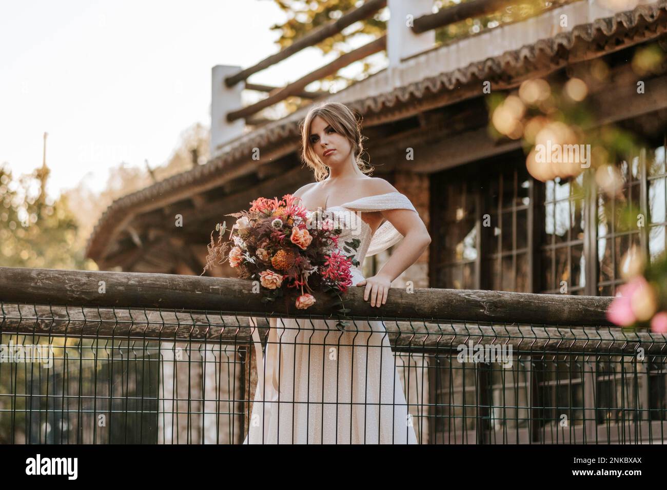 Beautiful bride standing on wooden rustic bridge over a river at sunset time Stock Photo