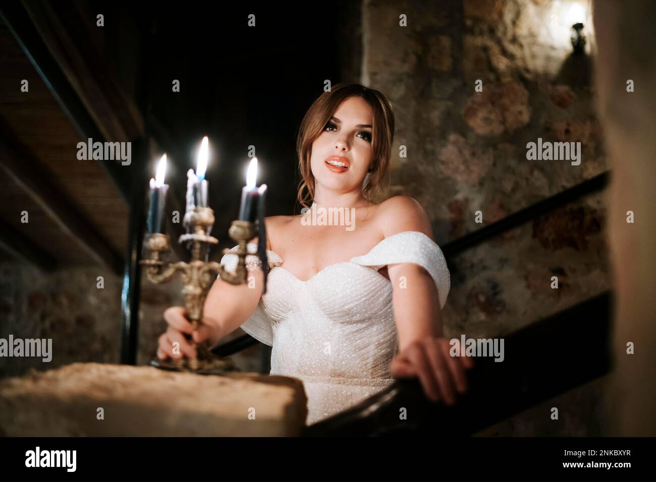 Portrait of beautiful bride holding candle in old stone rustic interior at night Stock Photo