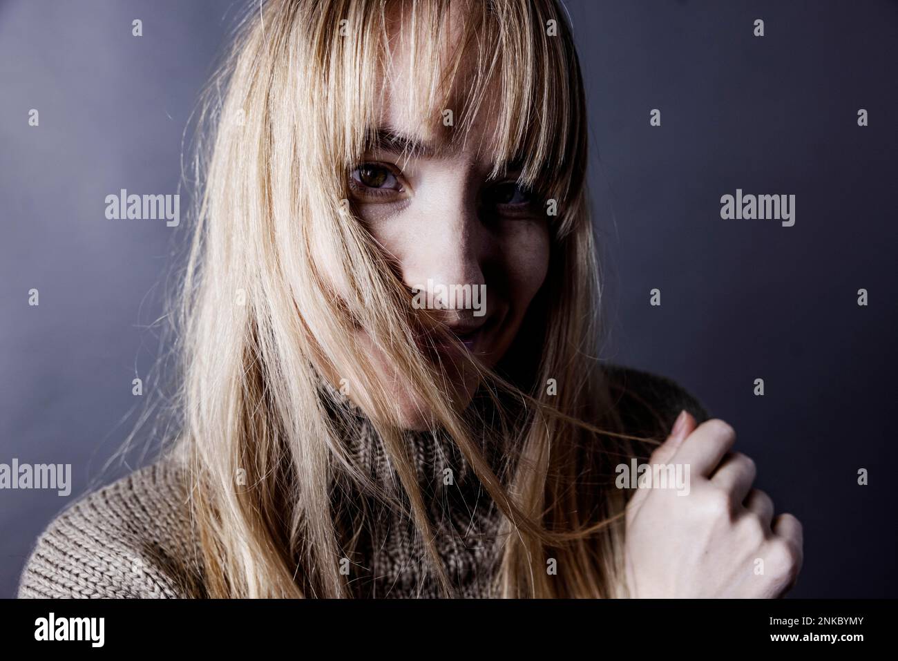 Young woman with long blond hair covers one half of her face with a strand of hair and looks saucily into camera, studio shot, Cologne, portrait Stock Photo