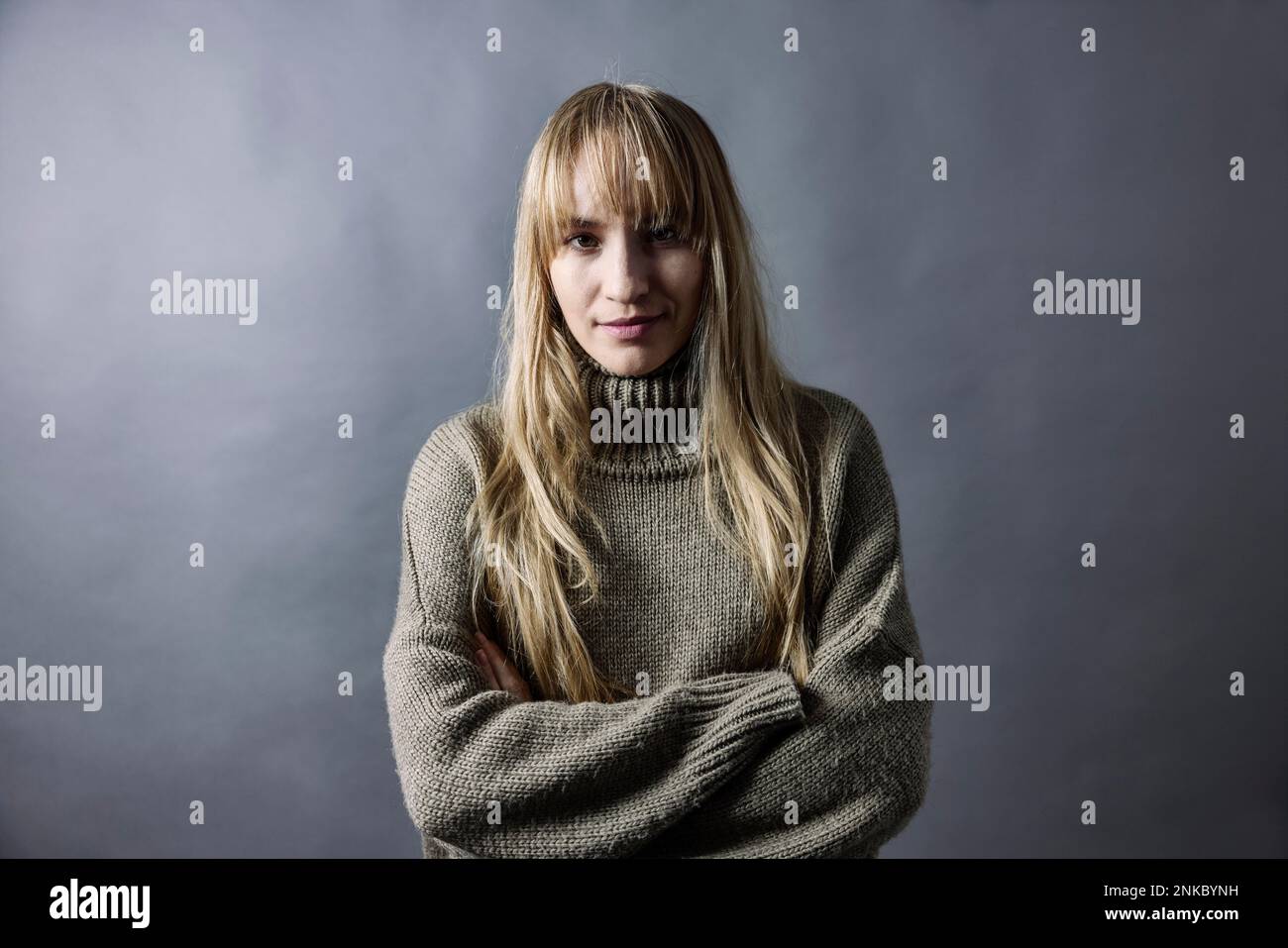 Woman with long blond hair and warm woollen jumper crosses her arms, portrait, studio shot Stock Photo