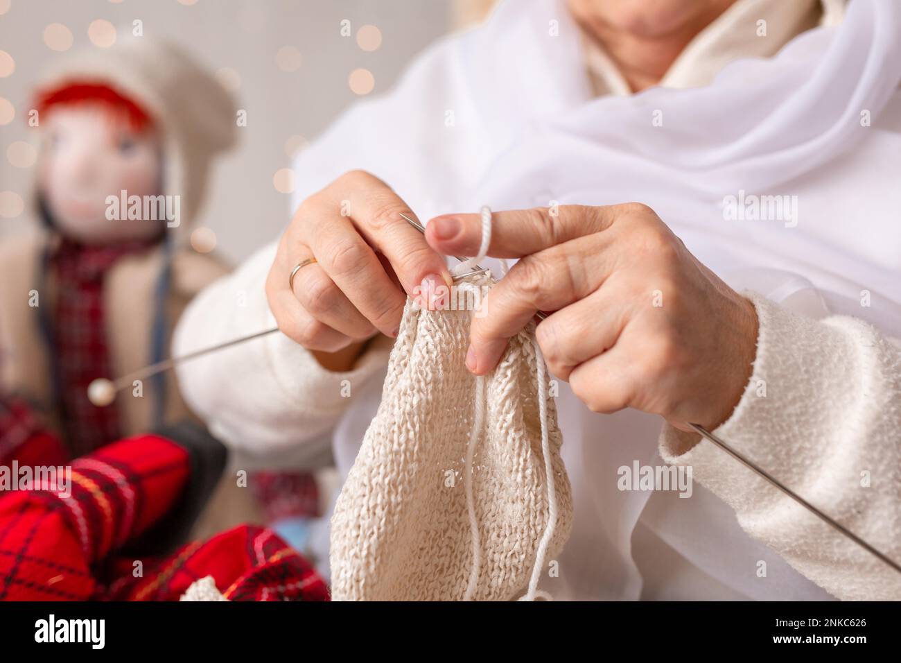 A nice elderly woman sews to knit her granddaughters in a Christmas arrangement. In studio Stock Photo