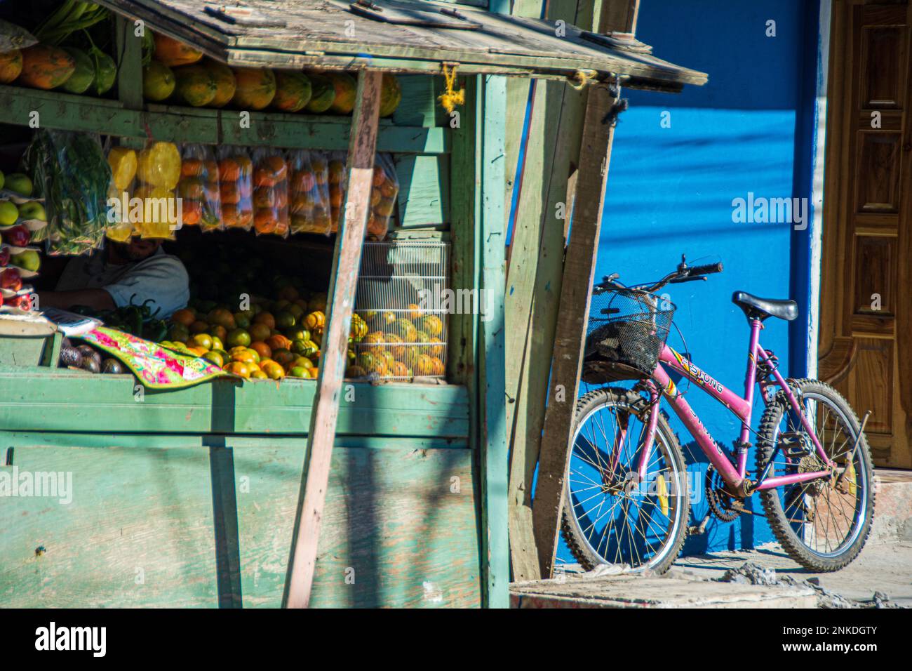 A fruit stand and a pink bike leaning against a blue wall of a building, Roatan, Honduras. Stock Photo