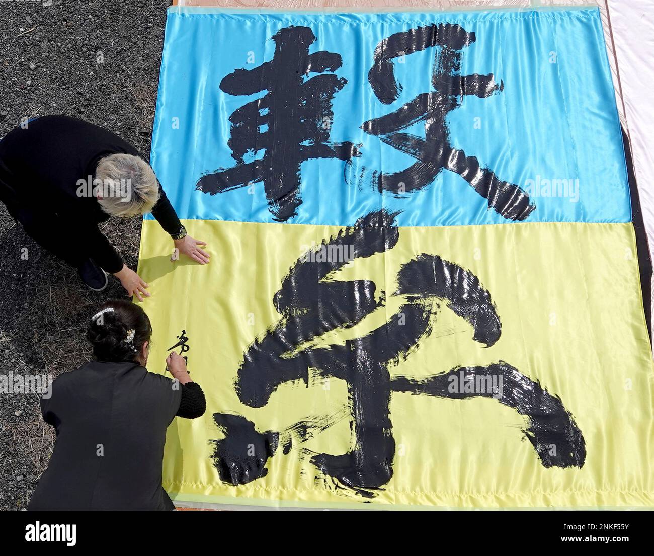 Hosui Ichinose (Left, below), a calligrapher writesthe Chinese character  Tsunagu, meaning connection or tie with a Ukrainian color in Toyota.  Aichi Prefecture on April 2, 2022. The event was held to support