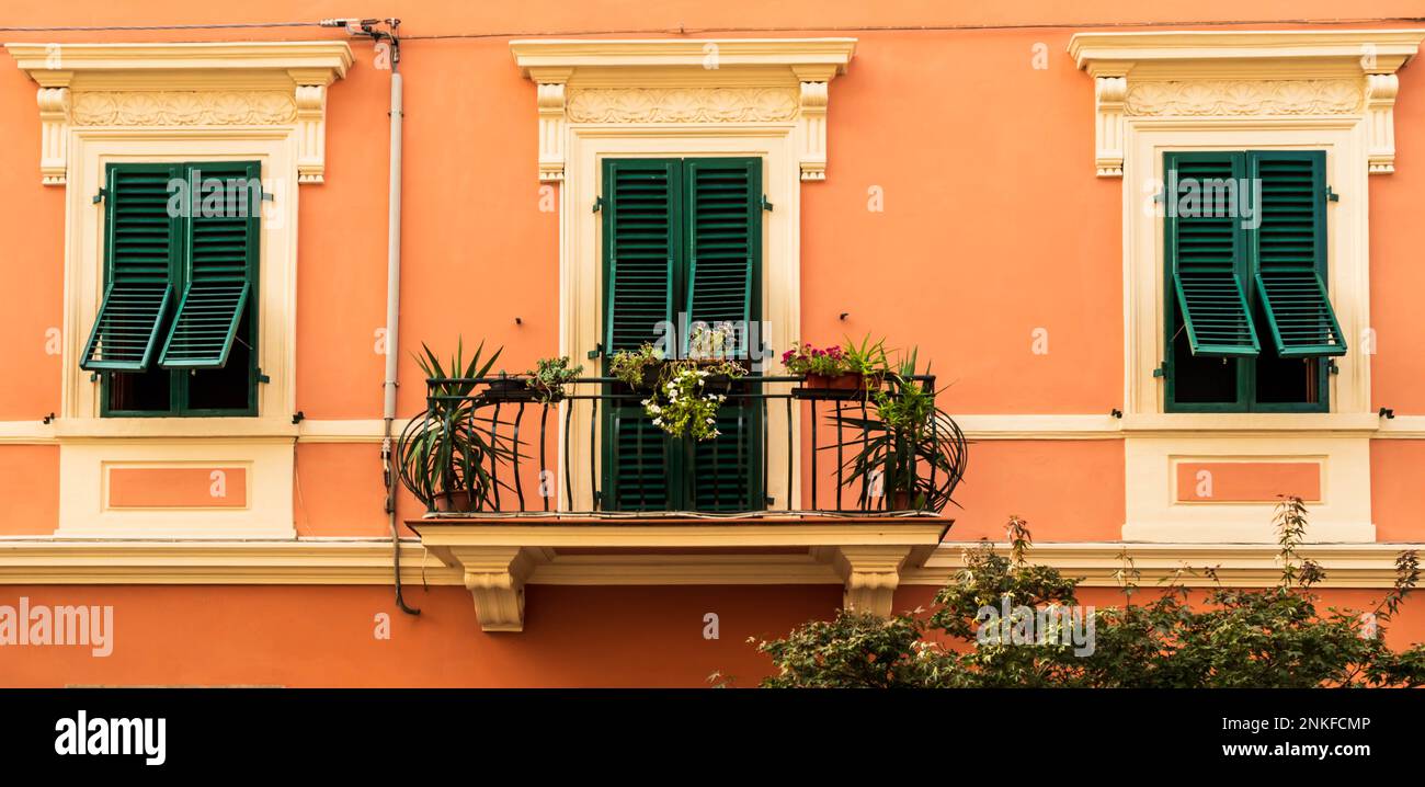 IItalian house with green shutters, ornate white window frames and apricot colored walls, with three windows and patio with iron railing. Stock Photo