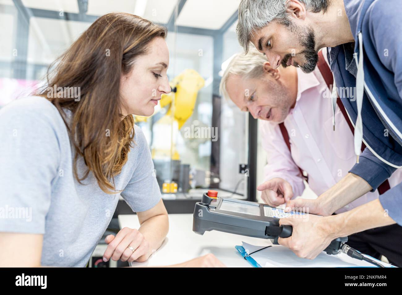 Colleagues watching woman programming robot arm with digital control Stock Photo