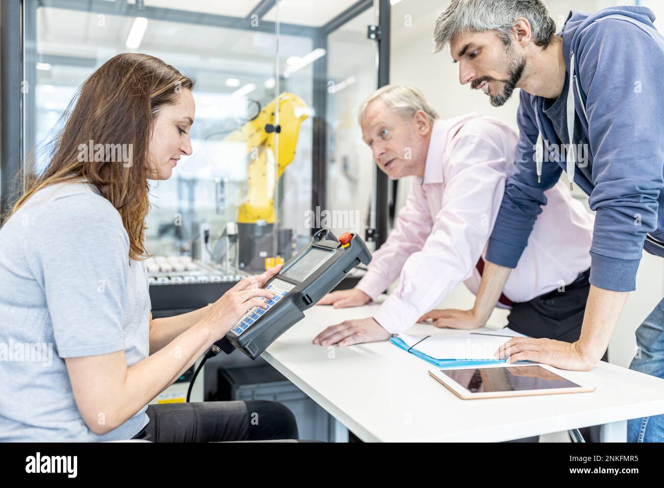 Colleagues watching woman programming robot arm with digital control Stock Photo