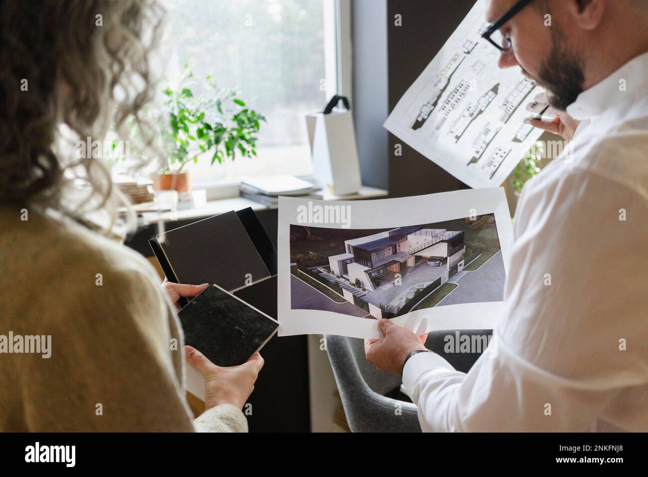 Two colleagues holding printout of a house and blueprint in architect's
