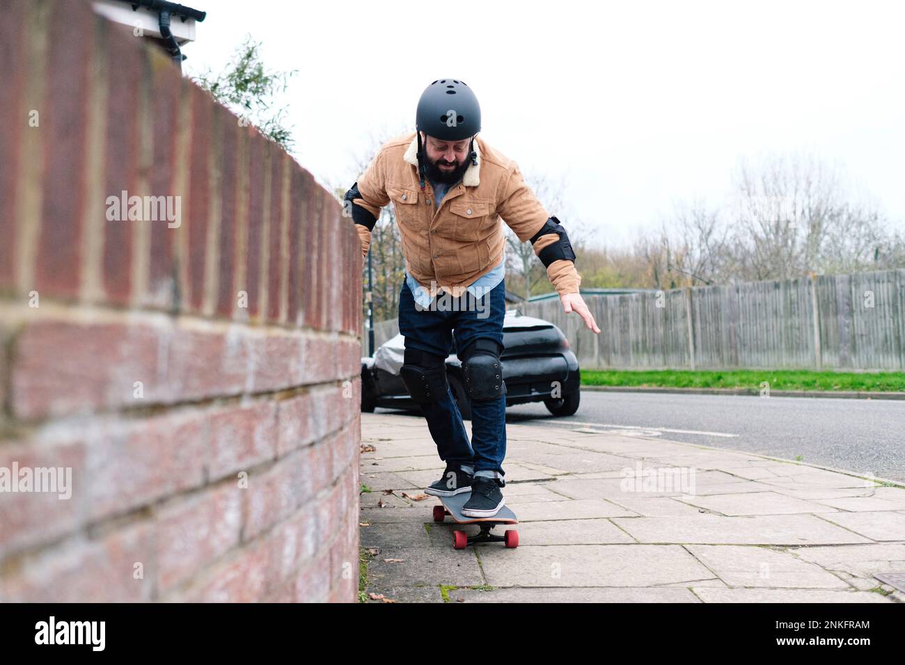 Mature man learning skateboarding taking support of wall on footpath Stock Photo