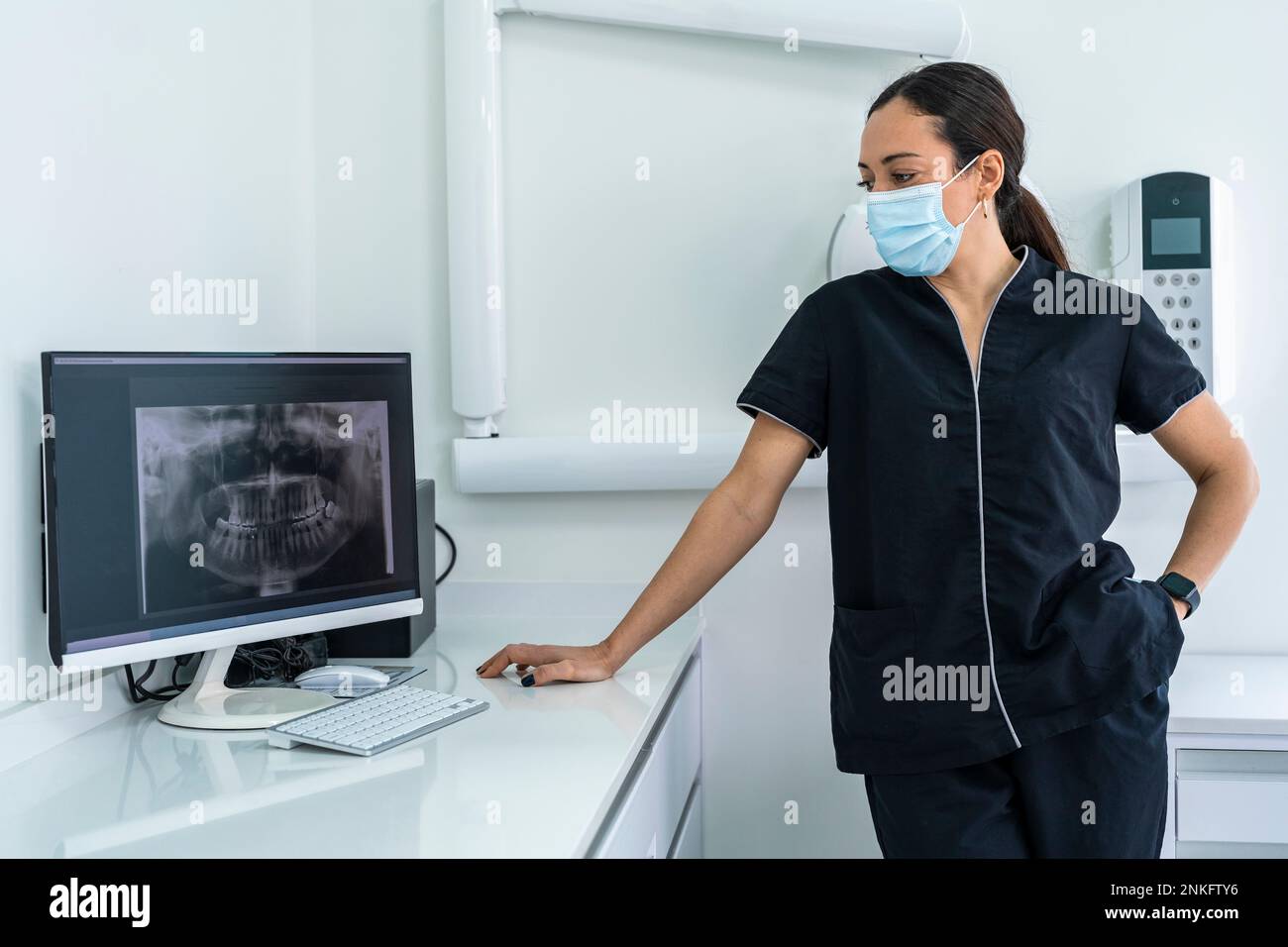 Doctor wearing surgical mask looking at X-ray image on computer at clinic Stock Photo