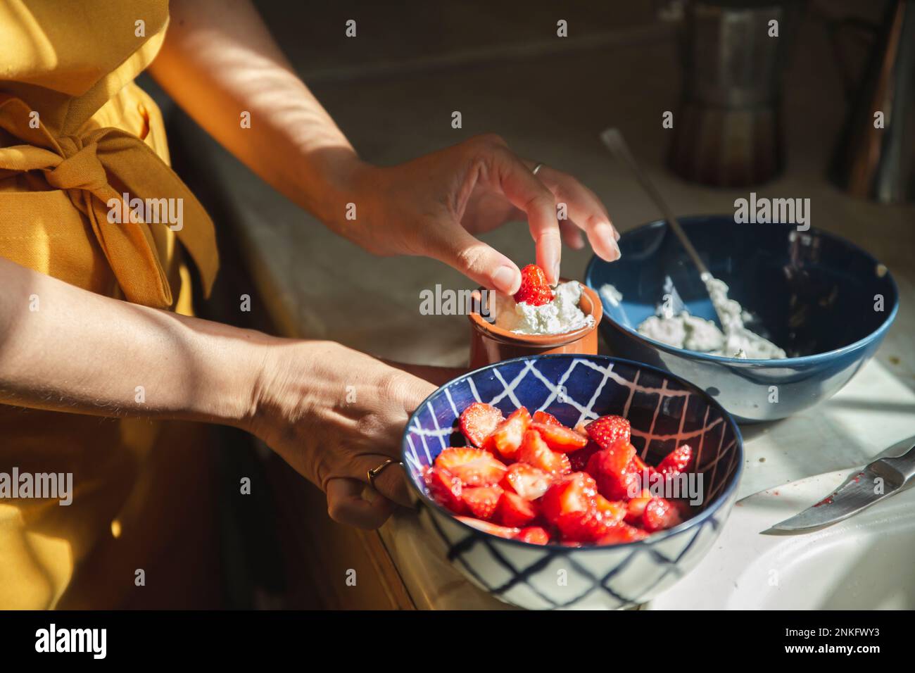 Hands of woman dipping strawberries in cream at kitchen Stock Photo