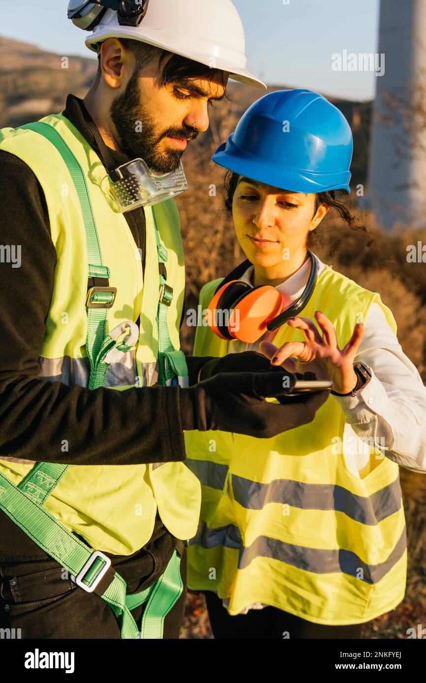 Engineer using smart phone with technician on sunny day Stock Photo