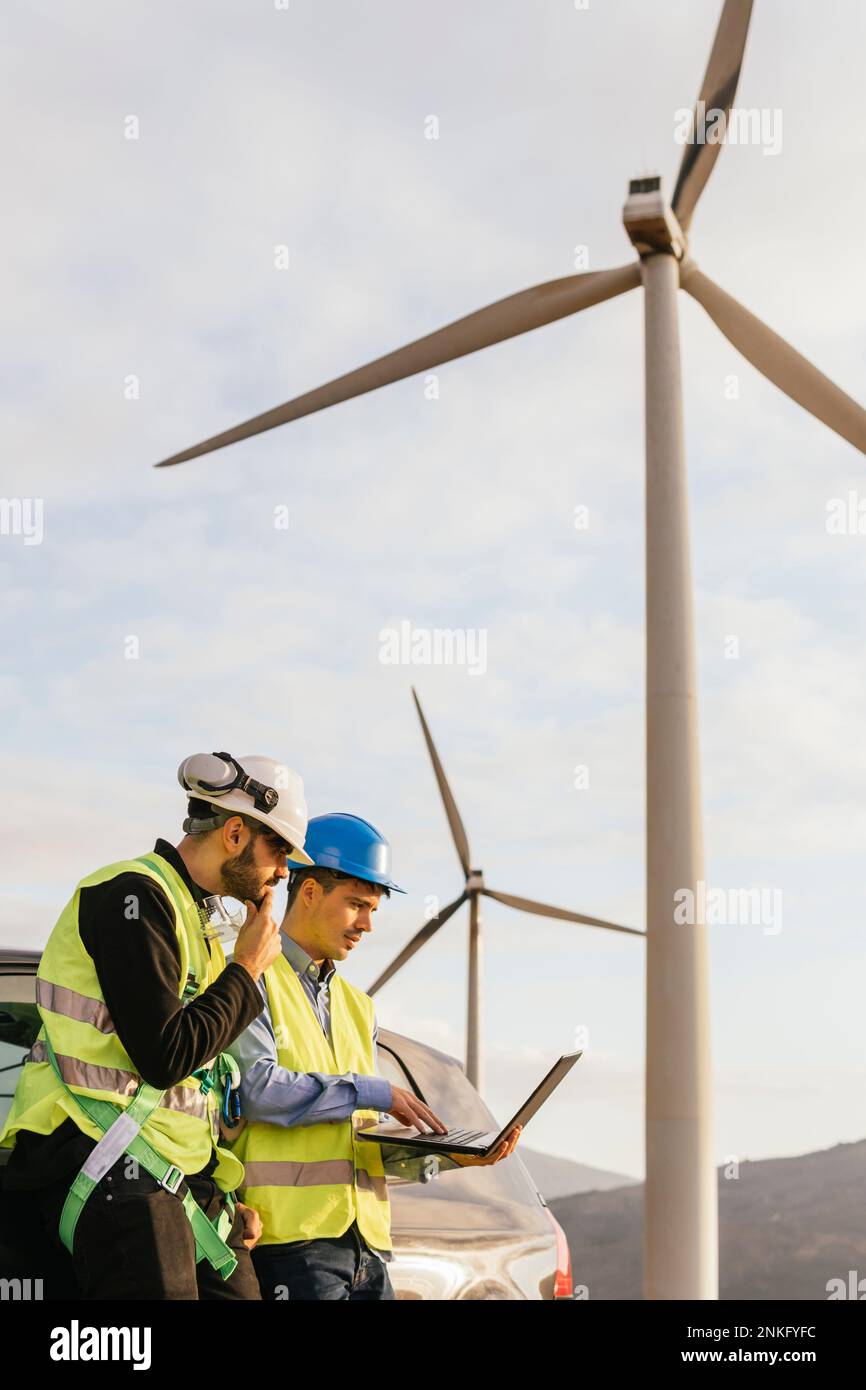 Technician and engineer working on laptop standing by car Stock Photo