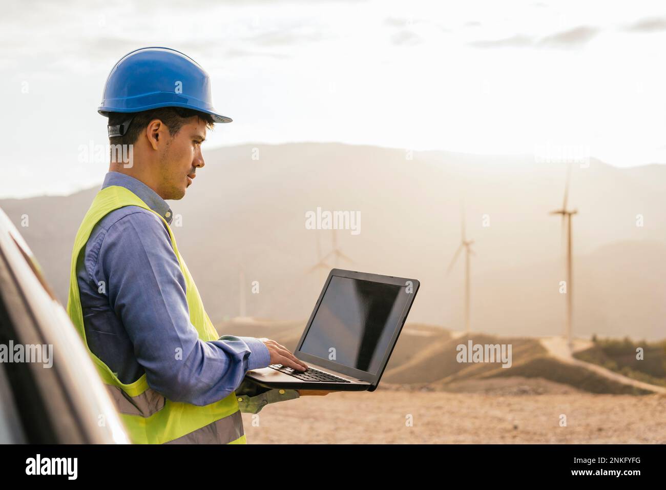 Engineer using laptop leaning on car in front of mountain Stock Photo